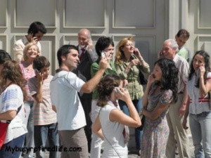 Crowd of people using cell phones in street, smiling
